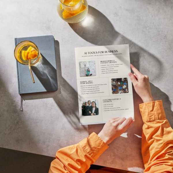Person holding a printed AI tools for business guide with a notebook and drink on the table